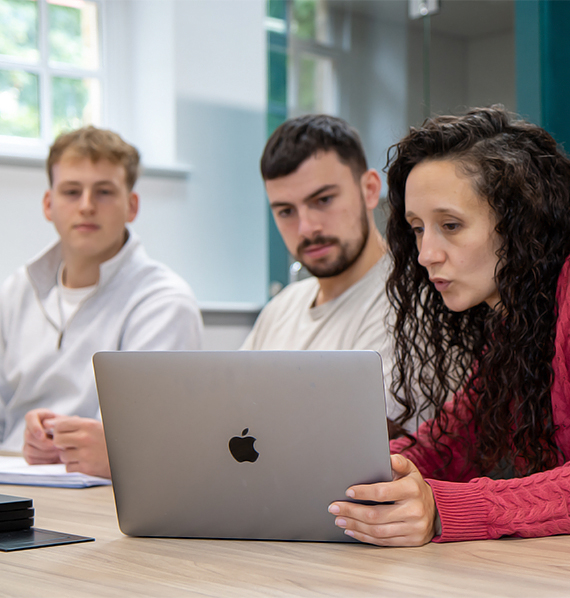 a group image of three individuals looking down at a laptop screen.