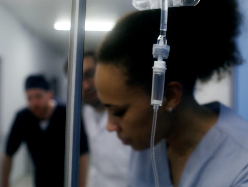 Medical staff pushing trolley with drip in foreground